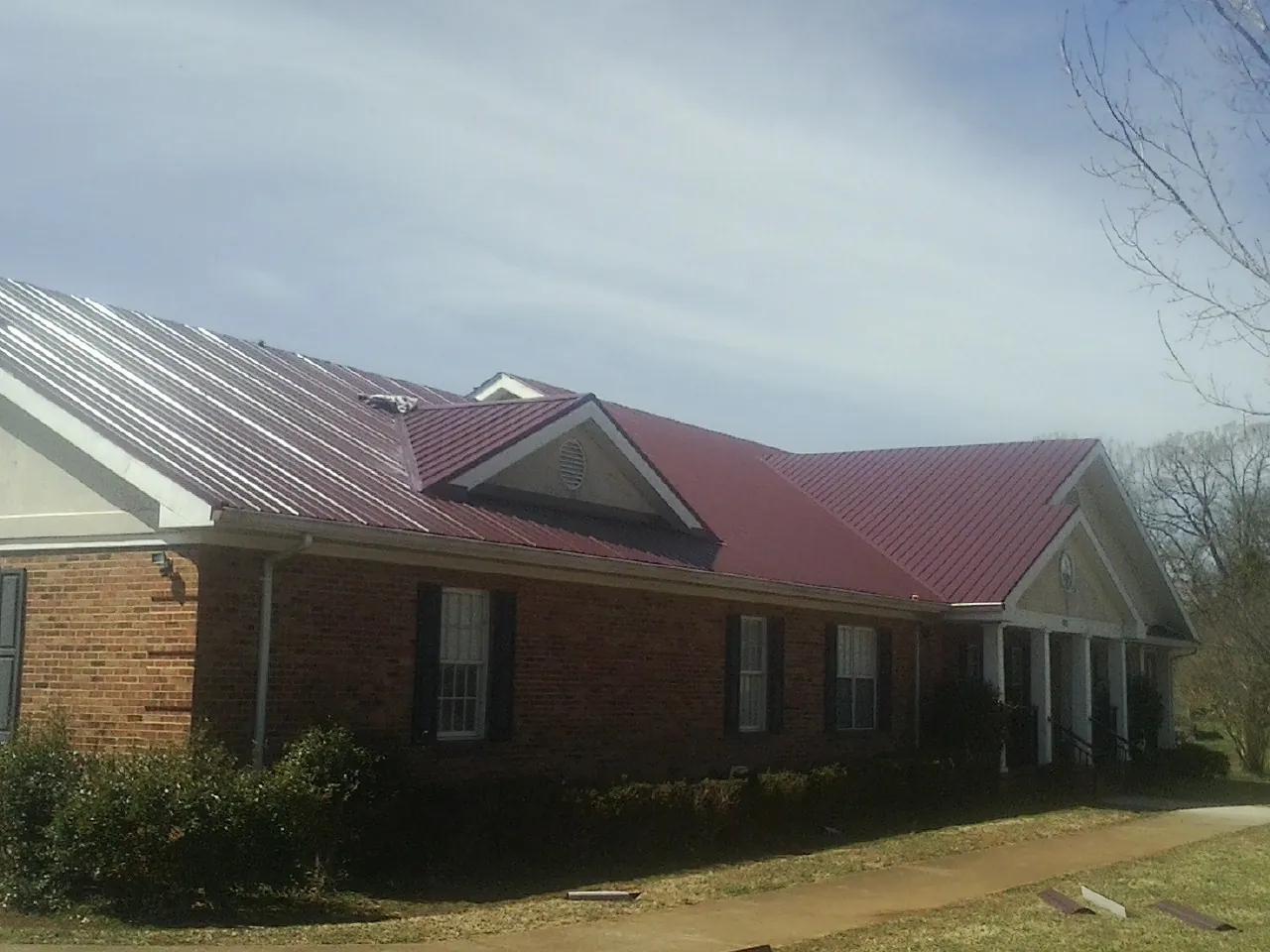 Red metal roof with gabled entries on a long brick building, from a Hail Damage Roof Repair job in Asheville