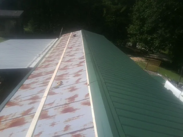 Old rusted panels beside newly installed green metal roofing — Wind Damage Roof Repair by Roofing Brothers in Asheville