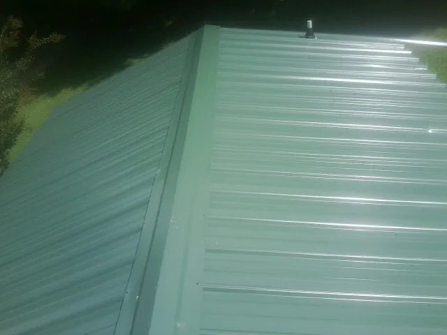 New green metal panels meeting at the ridge of a roof — Flat Roof Repair work by our crew in Asheville
