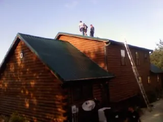 Crew on the ridge of a green metal roof on a two story log home in Asheville