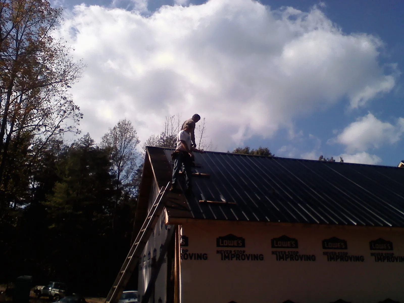 Roofer fastening dark metal panels high against a cloudy sky, from a Roof Inspection job in Asheville