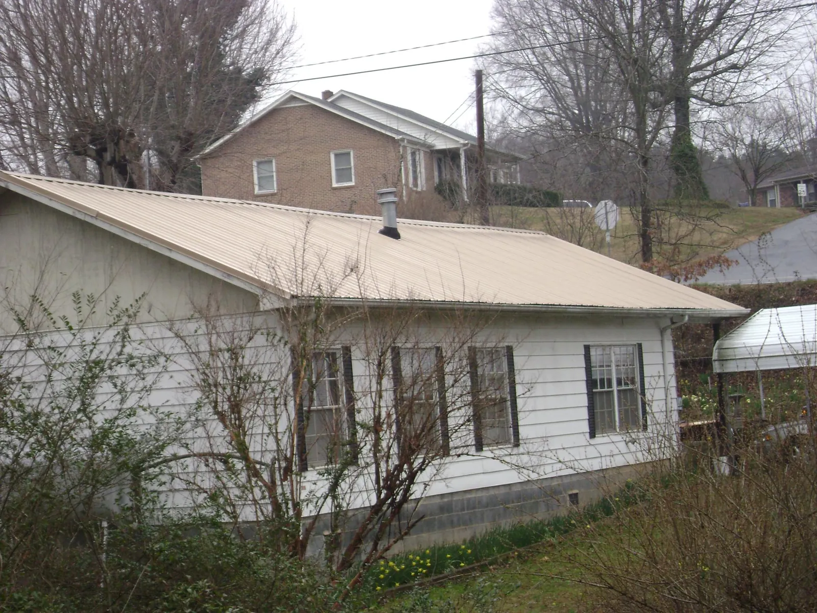 Tan metal roof on a white sided house set into a hillside — Commercial Roofing by Roofing Brothers in Asheville