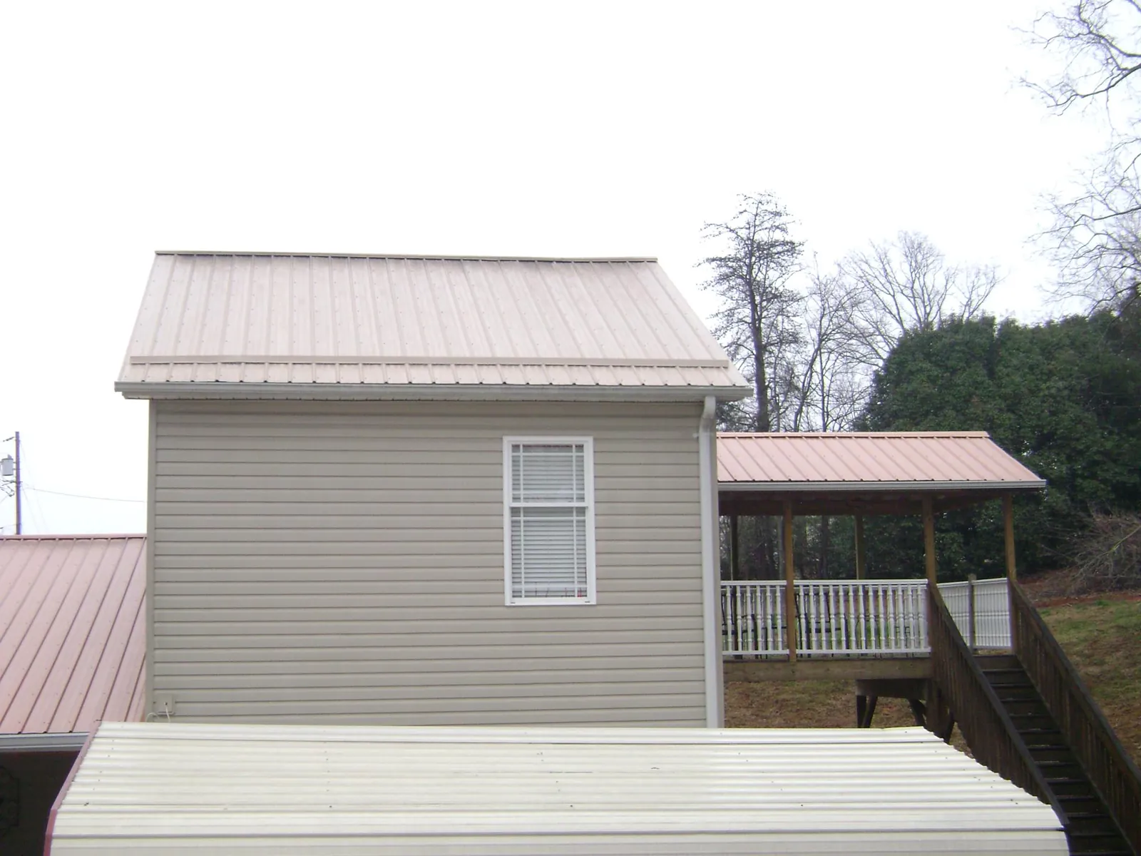 Tan metal roofs on a two story addition and attached porch, from a Roof Replacement job in Asheville